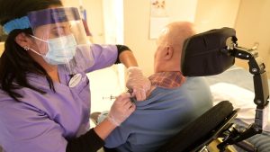 Nurse gives a long-term care resident in a wheelchair his COVID-19 vaccine