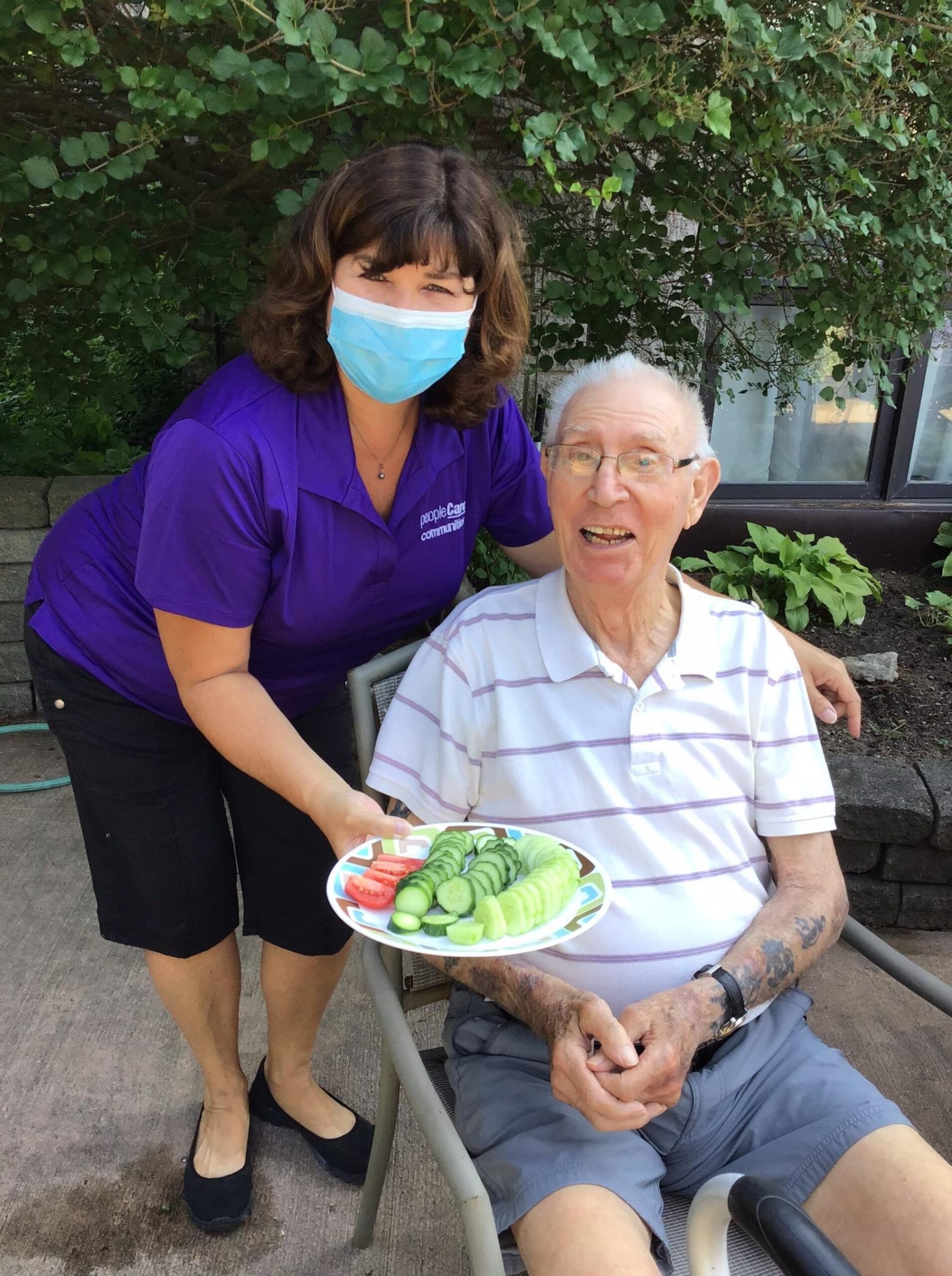 Staff member holding vegetables from the garden while standing next to a resident from a long-term care home