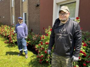 Two team members from Untapped Potential proudly stand next to the rose bushes.